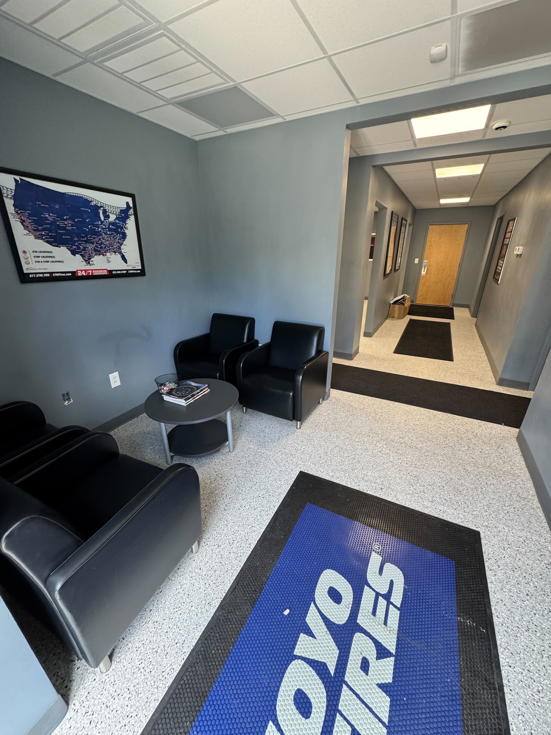 Waiting area with black chairs, a coffee table, and a map on the wall. The floor has a speckled patt