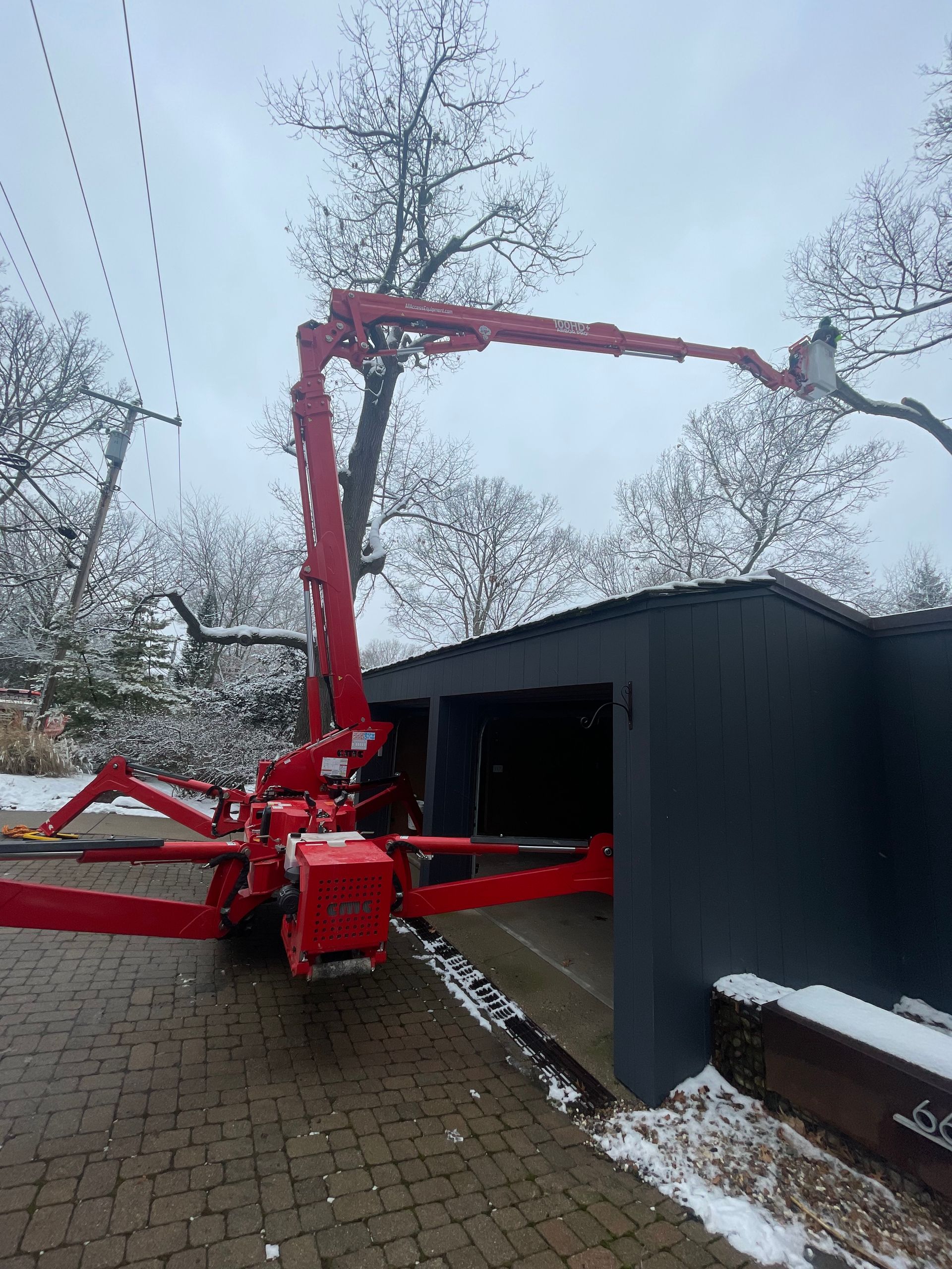 A red crane is cutting a tree in front of a garage.