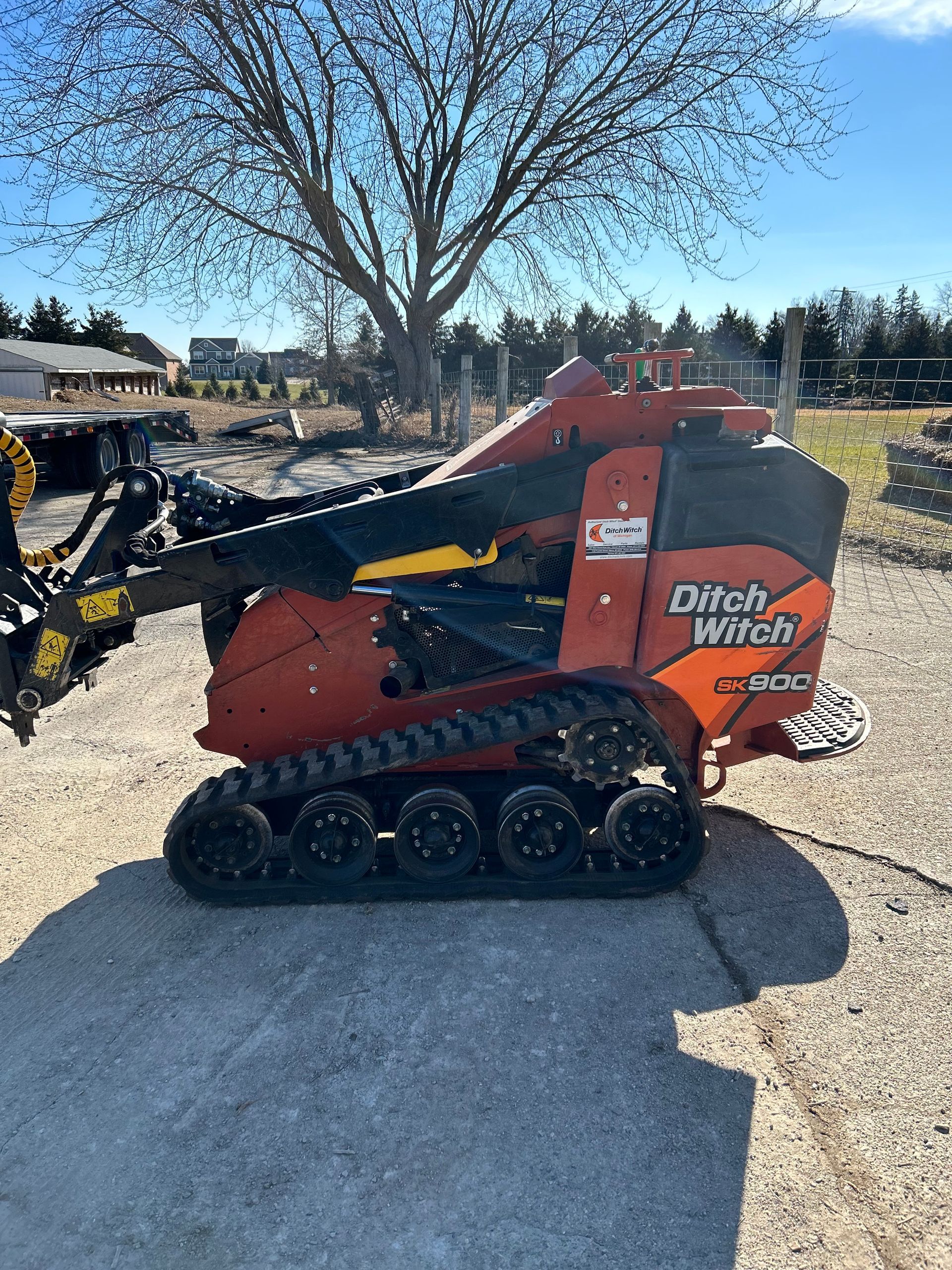 A small tractor is parked in a dirt lot next to a tree.