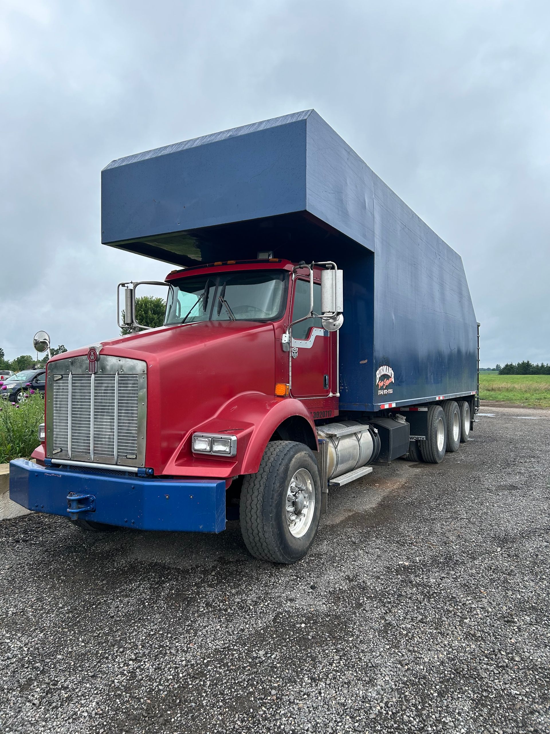 A red semi truck with a blue trailer is parked in a gravel lot.