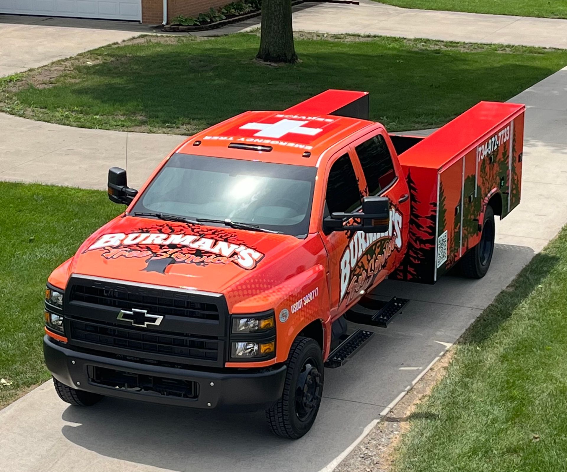 An orange truck with a trailer attached to it is parked on the side of the road.