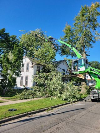 A green crane is cutting a tree in front of a house.