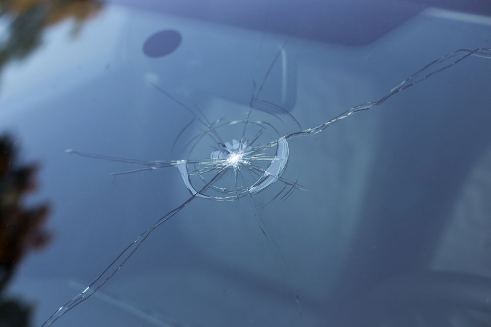 Close-up of a car windshield with a large circular crack and radiating fractures.