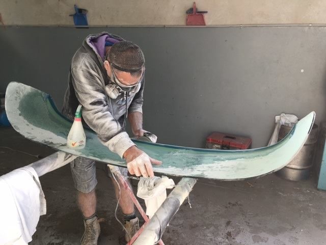 Man Wearing Safety Glasses Sanding A Green Curved Object In A Workshop