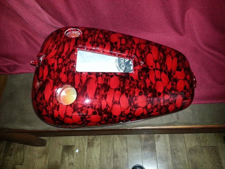 A red motorcycle tank is sitting on a wooden table.