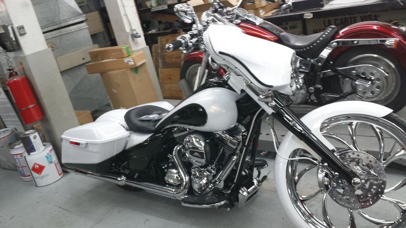 A white motorcycle is parked next to a red motorcycle in a garage.