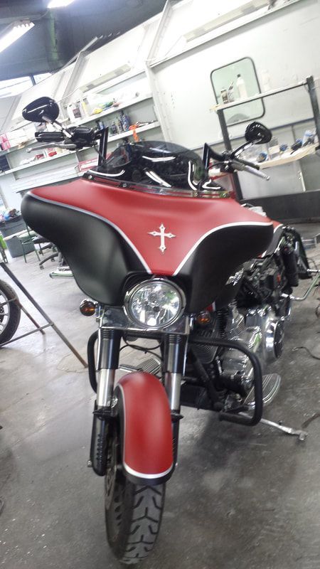 A red and black motorcycle with a cross on the front is parked in a garage.