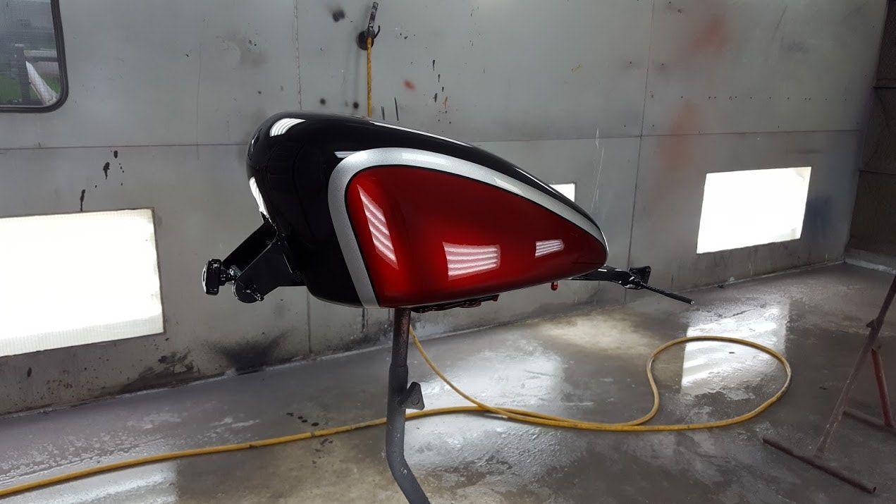 A red and black motorcycle tank is sitting on a stand in a room.