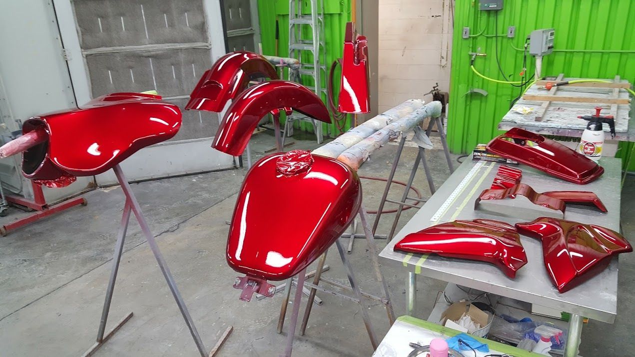 A motorcycle is being painted red in a garage.