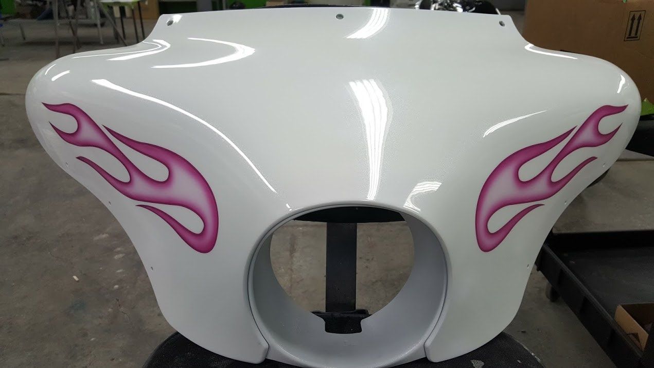 A white motorcycle windshield with pink flames painted on it