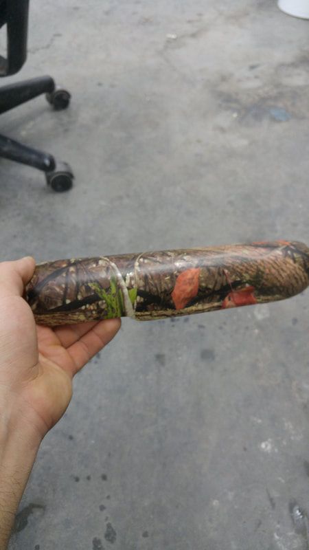 A person is holding a camouflaged sausage in their hand.