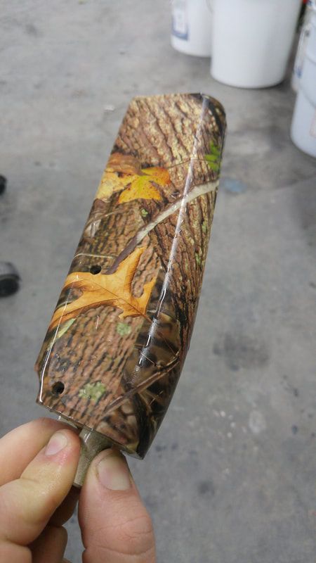 A person is holding a piece of wood with a camouflage pattern on it.