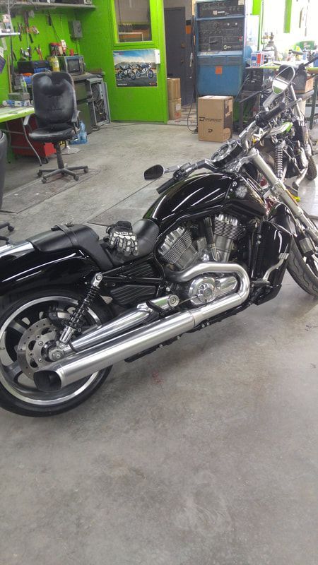 A black motorcycle is parked in a garage next to another motorcycle.
