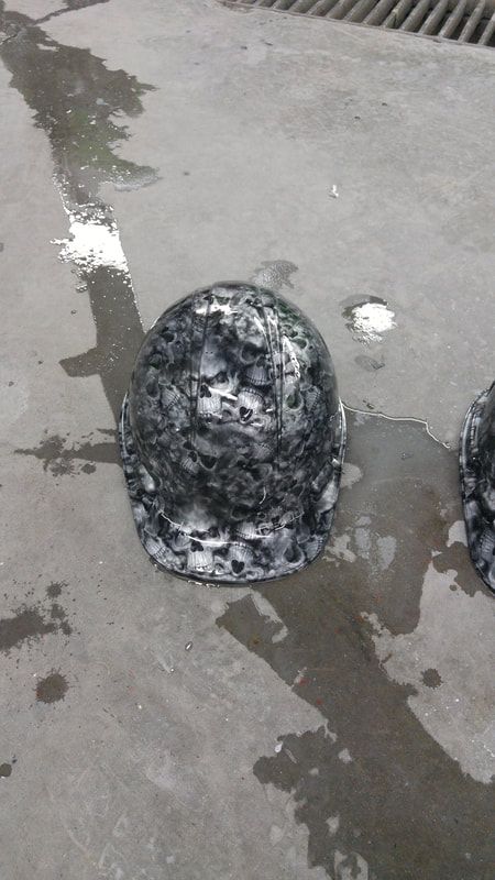 Two hard hats with skulls painted on them are sitting on the ground.