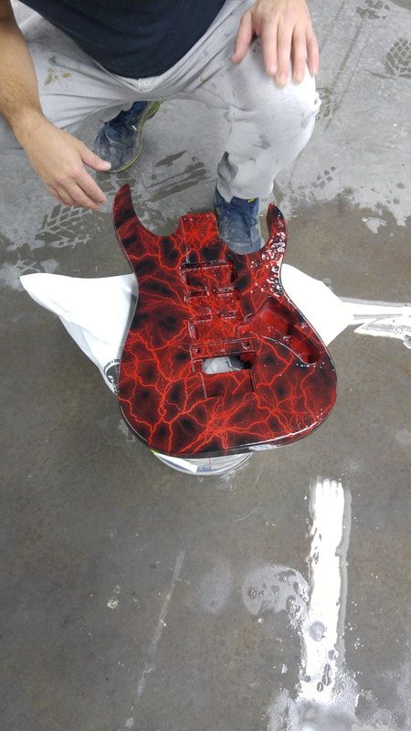 A man is kneeling down next to a red and black electric guitar.