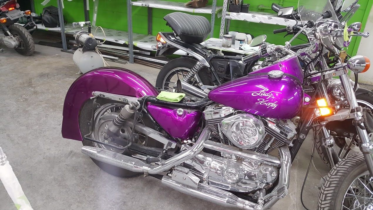 A purple motorcycle is parked in a garage next to other motorcycles.