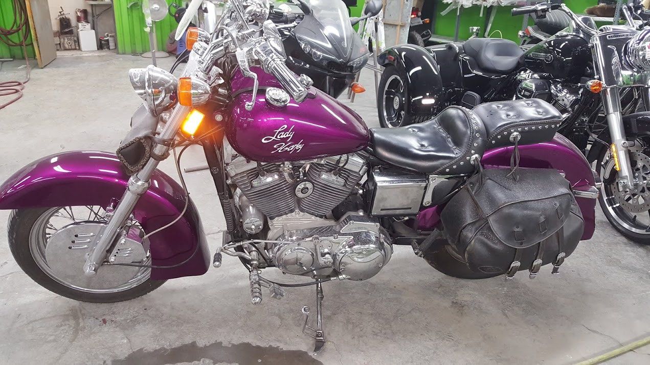 A purple motorcycle is parked in a garage next to other motorcycles.