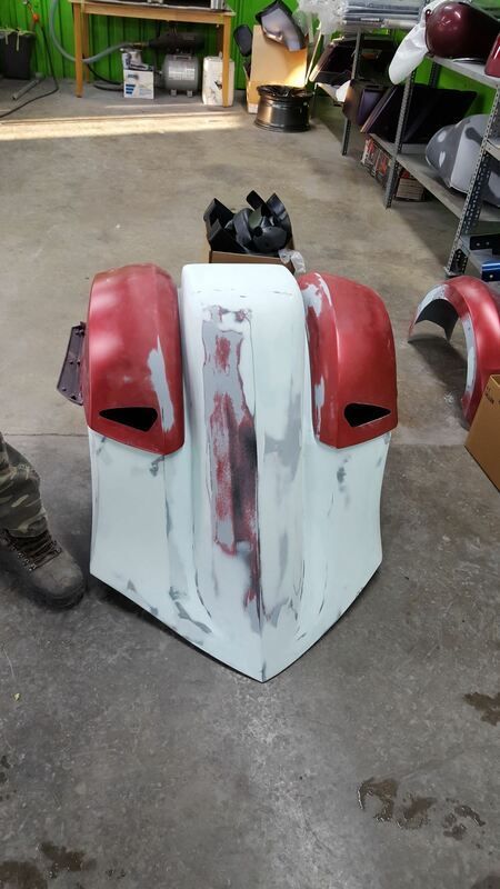 A white and red motorcycle fender is sitting on the floor in a garage.