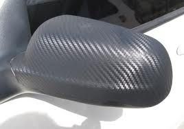 A close up of a car 's side mirror with carbon fiber wrapping.