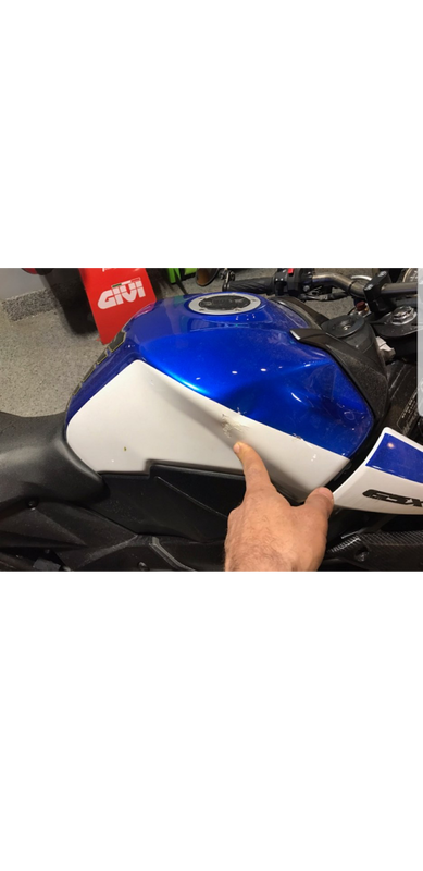 A person is pointing at the side of a blue and white motorcycle.