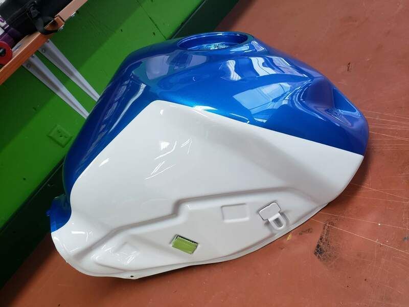 A blue and white motorcycle tank is sitting on the floor