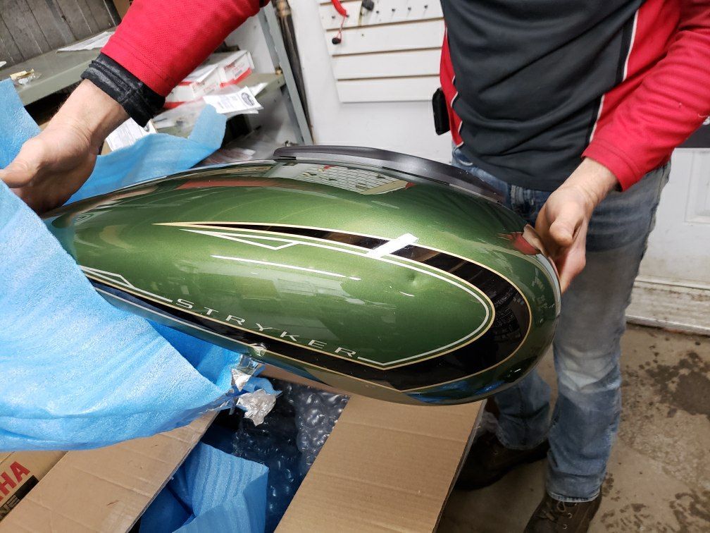 A man in a red jacket is holding a green motorcycle tank