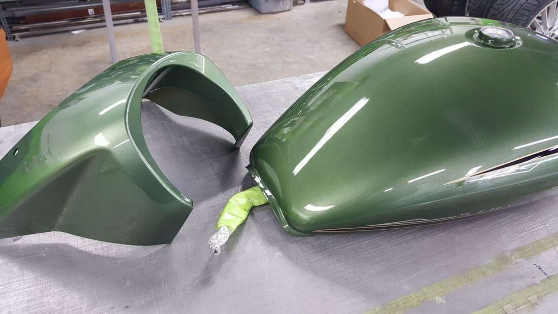 A green motorcycle tank and fender are sitting on a table.