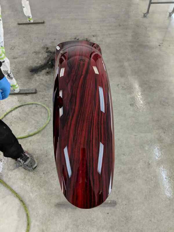 A red motorcycle fender is being painted in a garage.