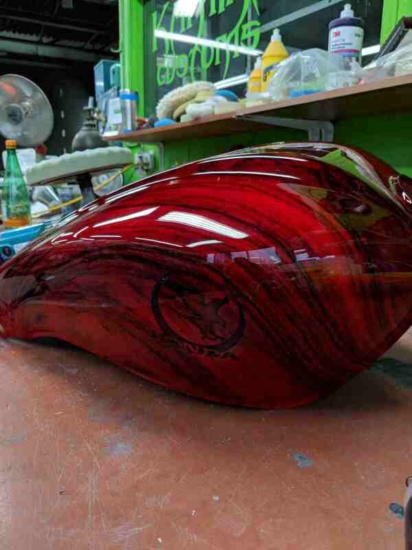 A red motorcycle tank is sitting on a table in a garage.