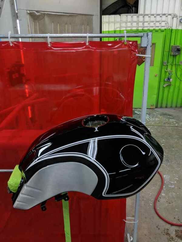 A black motorcycle tank is sitting in front of a red curtain.