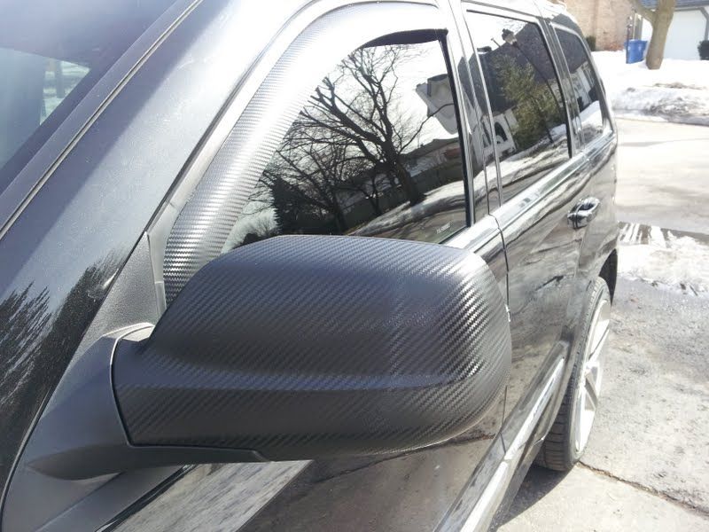 A black car with a carbon fiber wrap on the side mirrors