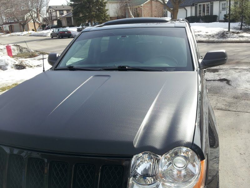 A black jeep is parked in a driveway with snow on the ground