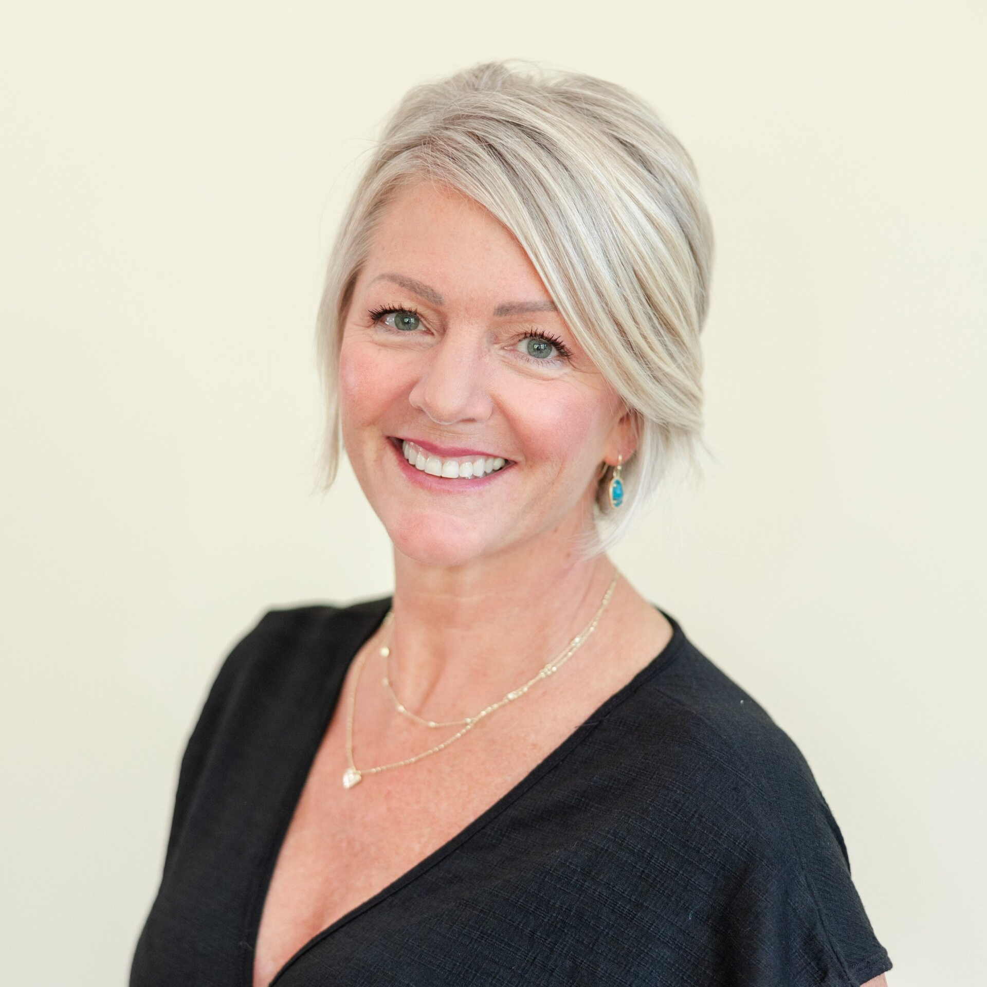 A woman wearing a black shirt and a necklace is smiling for the camera.