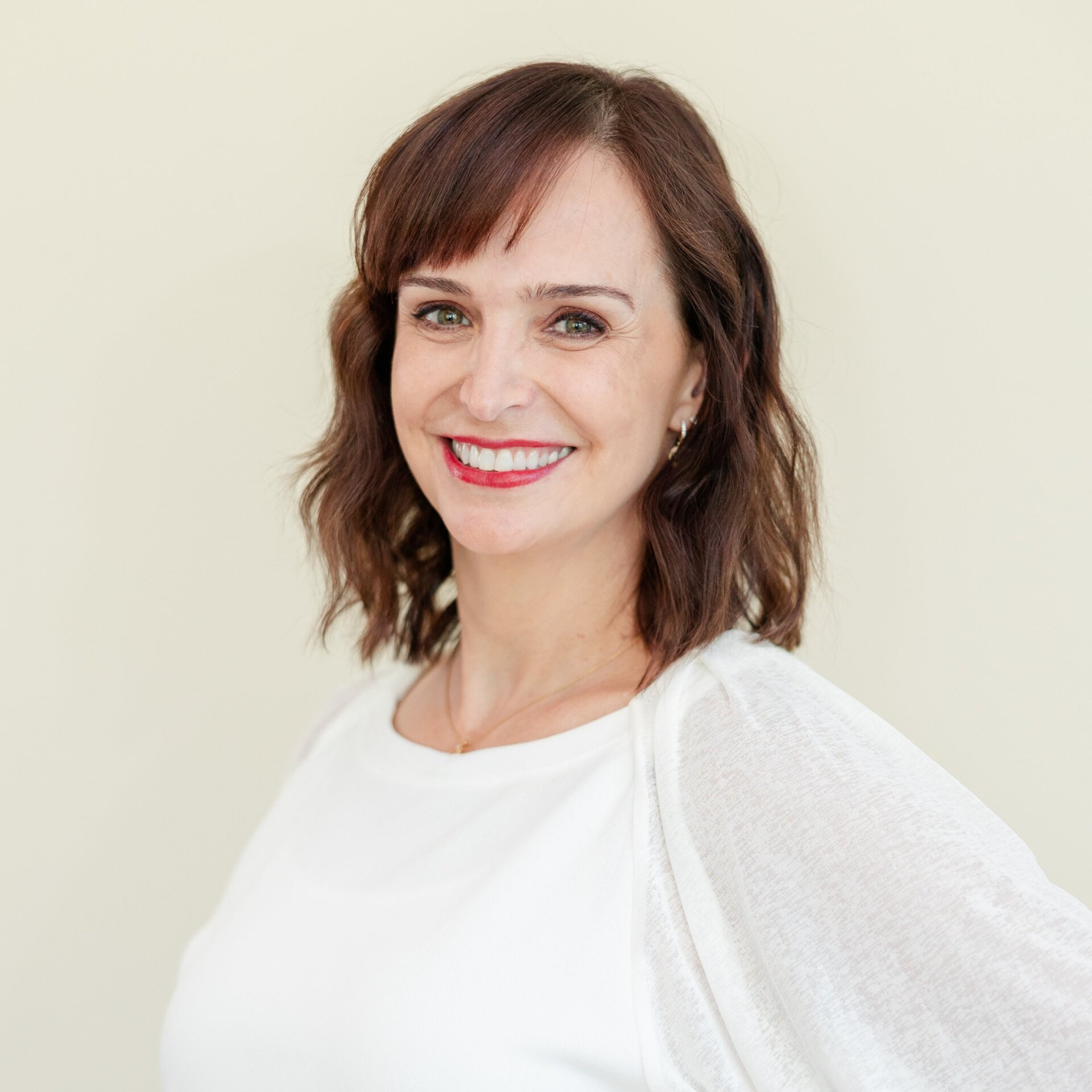A woman wearing a white shirt and red lipstick is smiling for the camera.