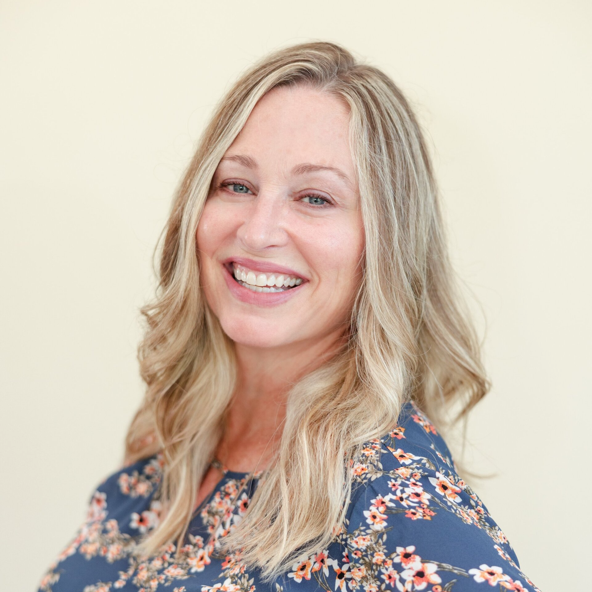A woman in a blue floral shirt is smiling for the camera.