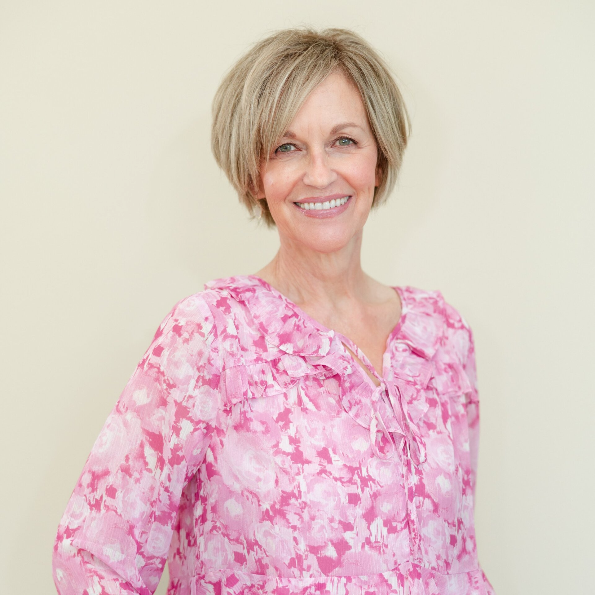 A woman in a pink floral shirt is smiling for the camera.