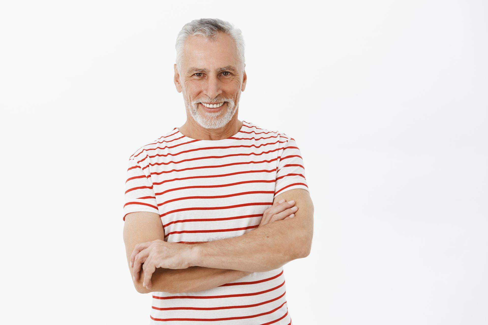 A man in a striped shirt is standing with his arms crossed and smiling.