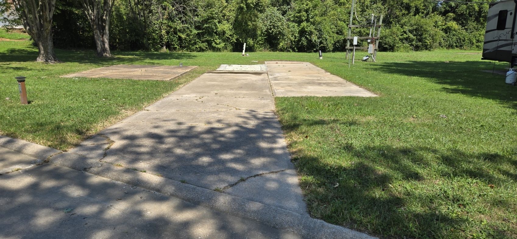 A concrete driveway leading to a grassy field with a trailer parked in the background.