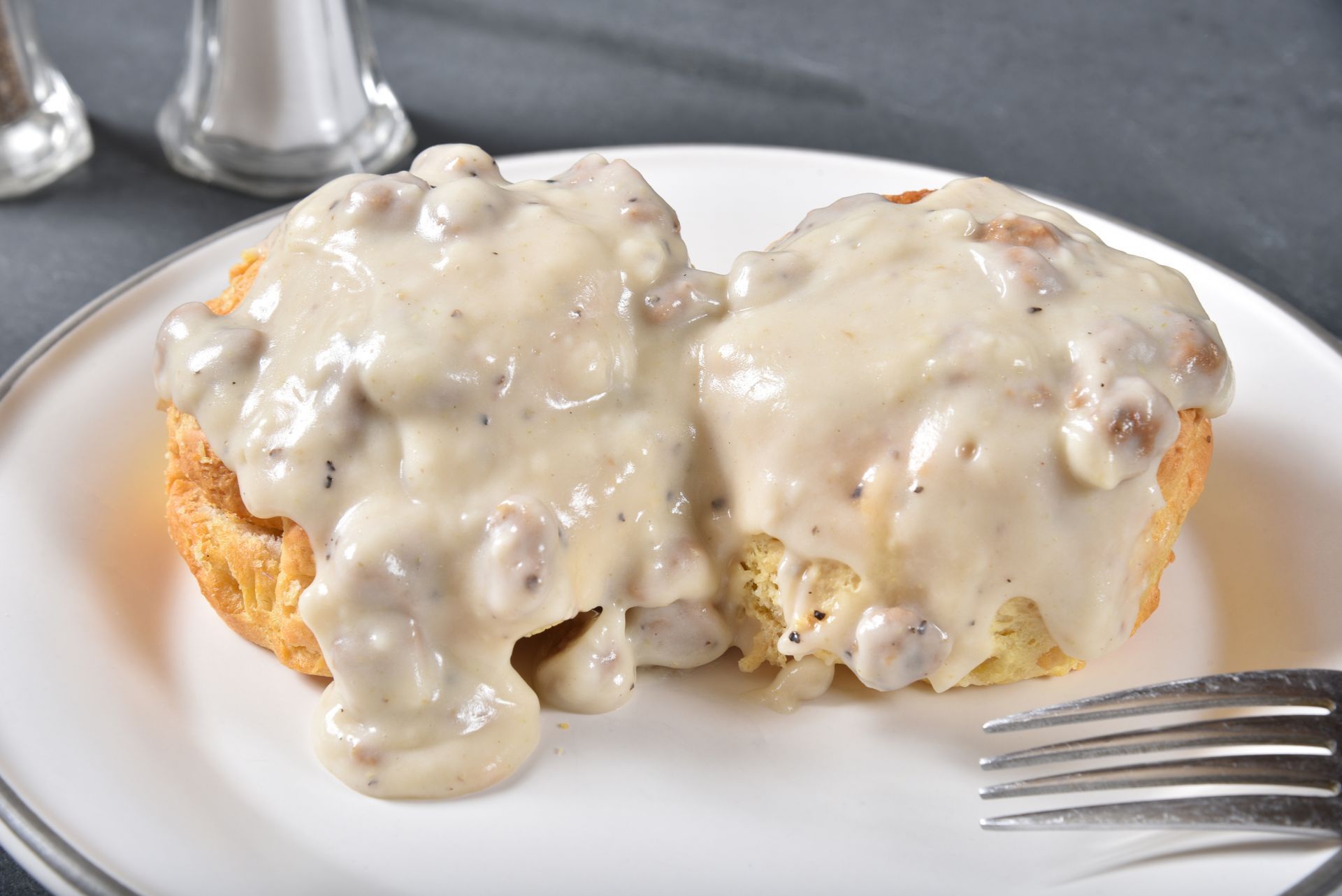 Two biscuits covered in gravy on a white plate with a fork.