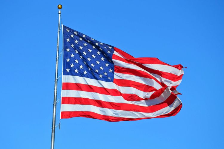 The American flag is waving in the wind against a blue sky.