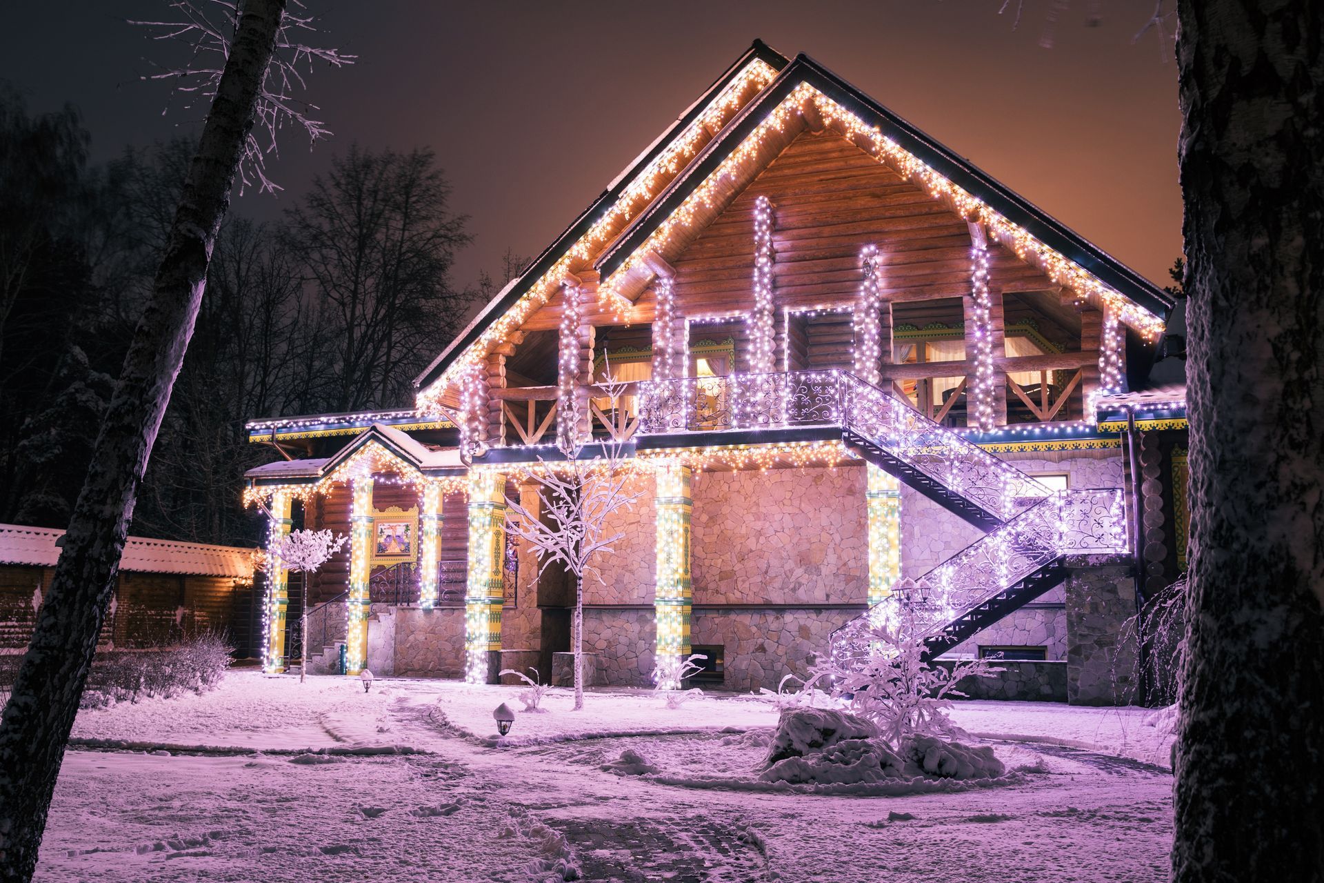 Snow-covered house outlined with pink and white holiday lights at night