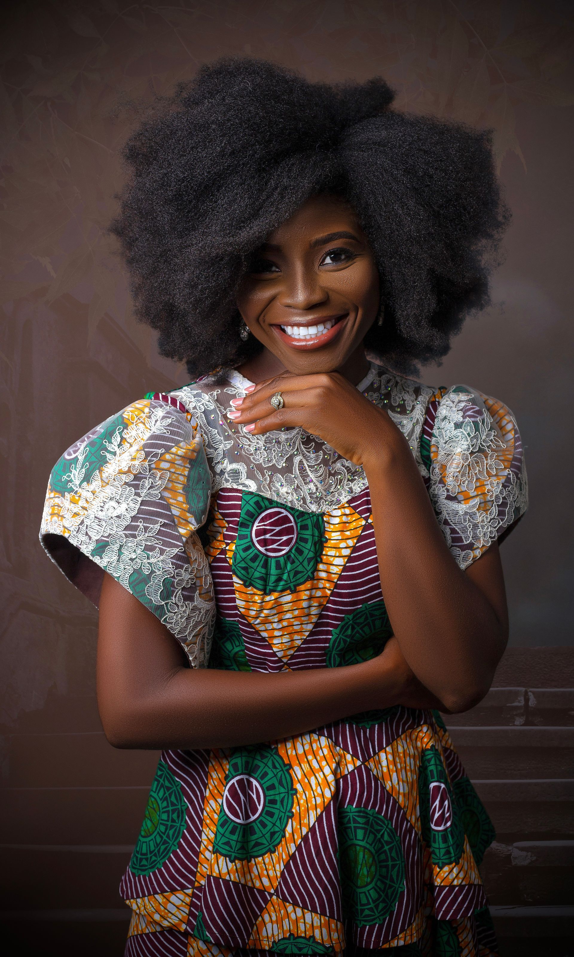 A woman with afro hair is wearing a colorful dress and smiling.