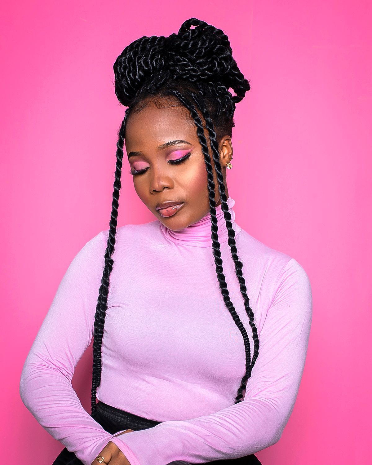 A woman with braids is wearing a pink turtleneck sweater.