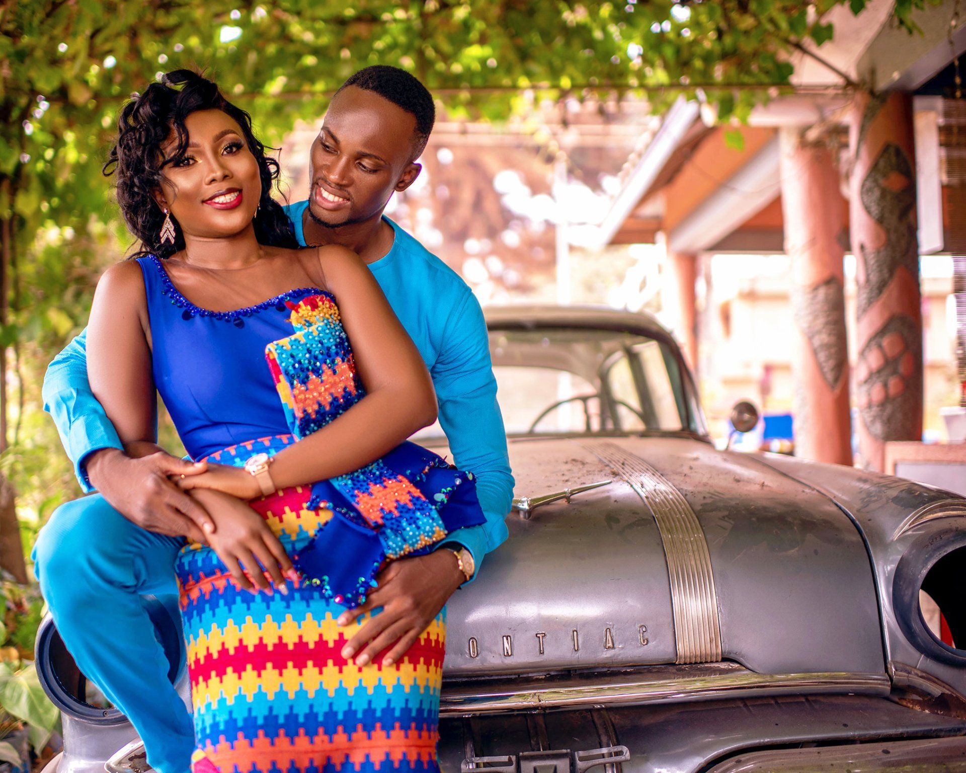 A man and a woman are sitting on the hood of a car.