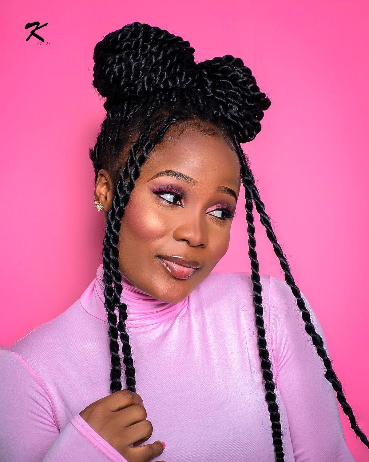A woman with braids in a bun is wearing a pink shirt.