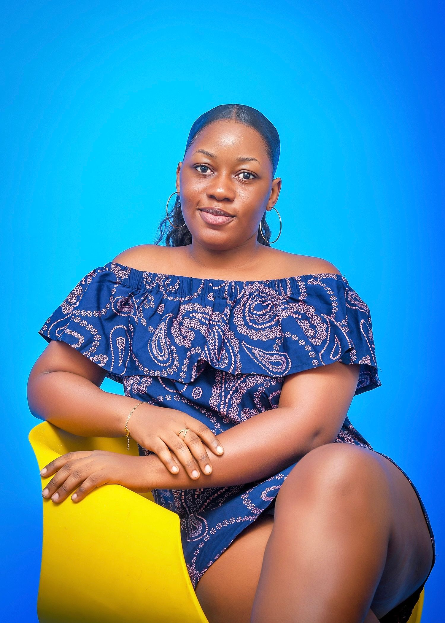 A woman in a blue dress is sitting on a yellow chair.