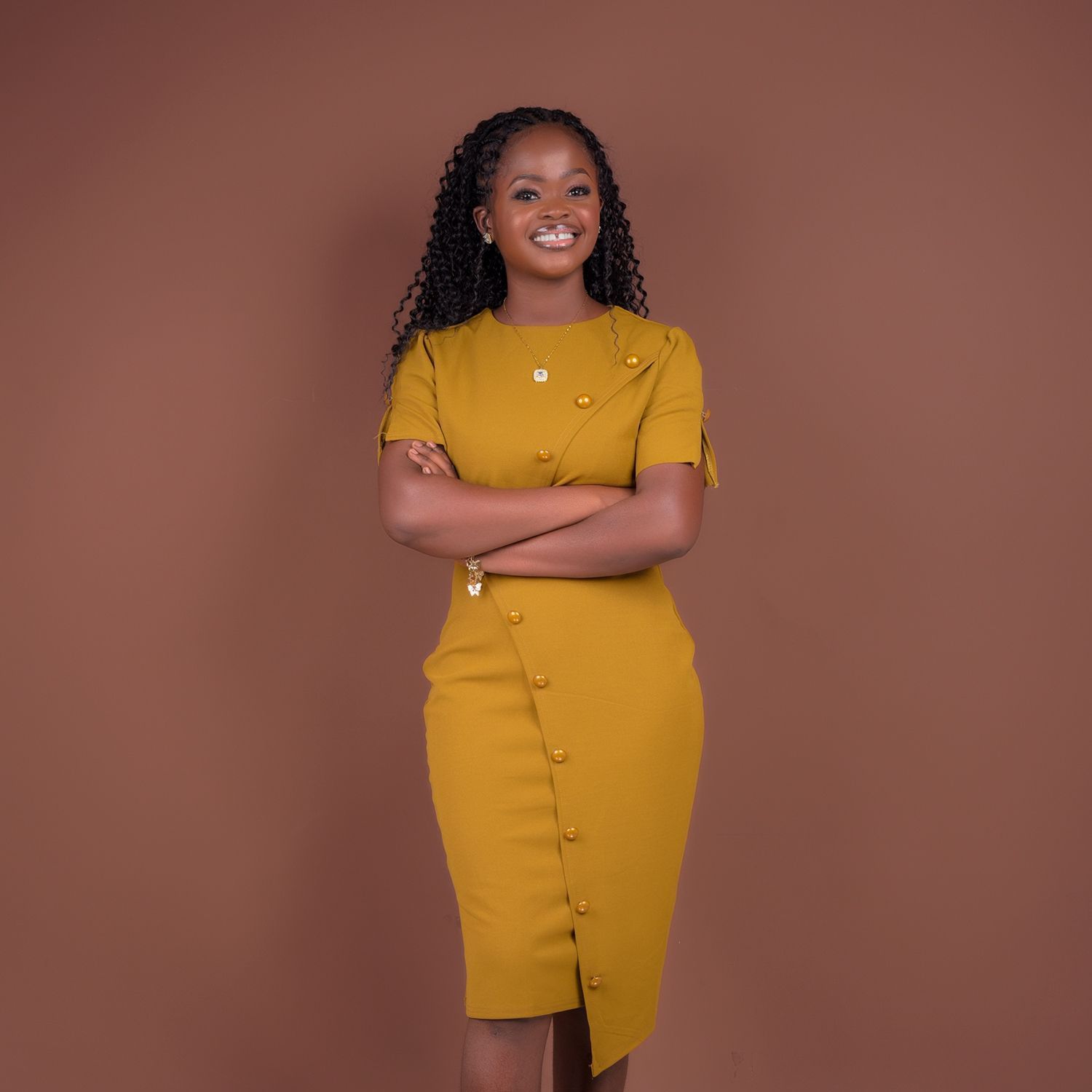 A woman in a yellow dress is standing with her arms crossed.