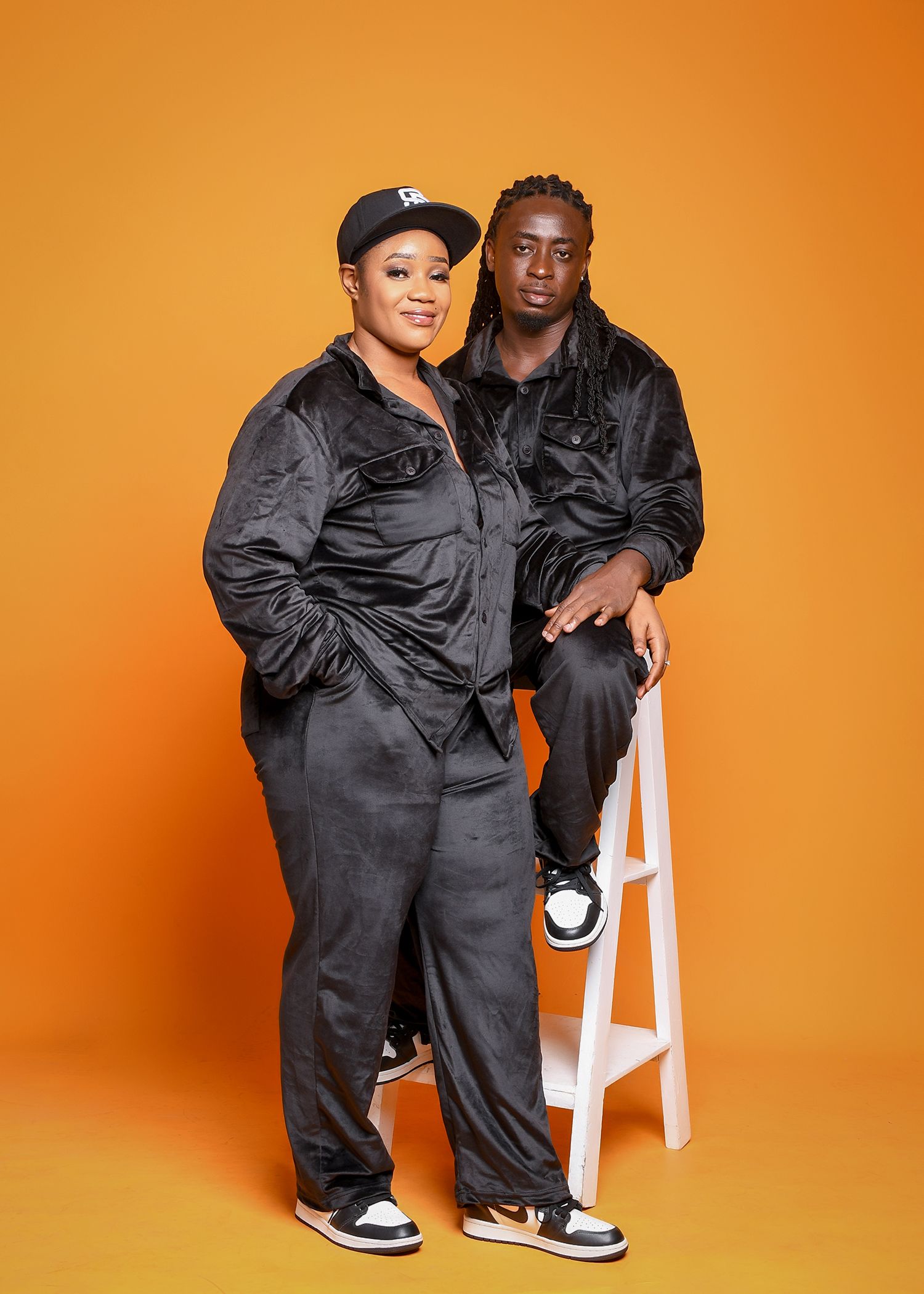 A man and a woman are standing next to each other in front of an orange background.