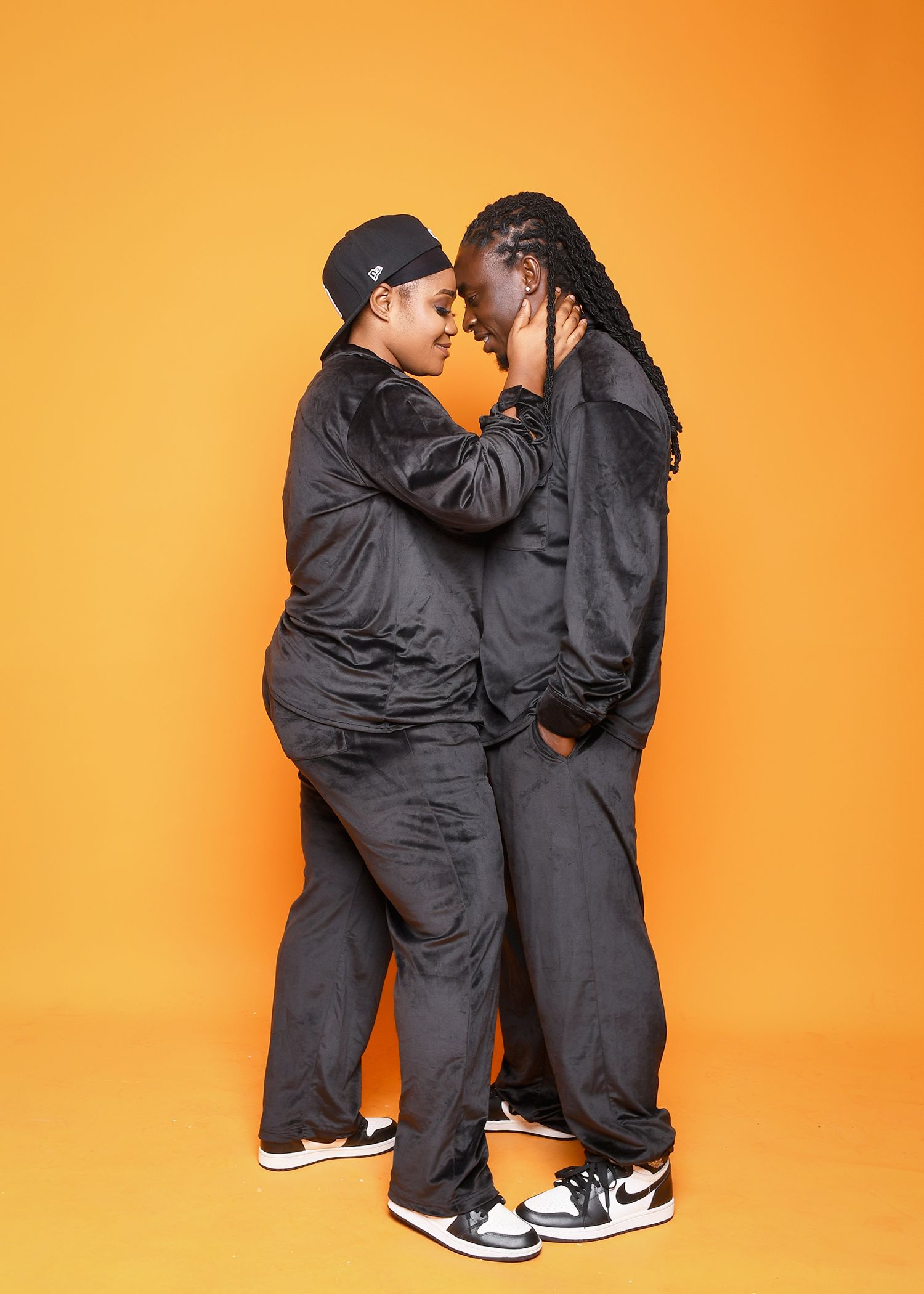 Two people in black clothes are standing next to each other on an orange background.