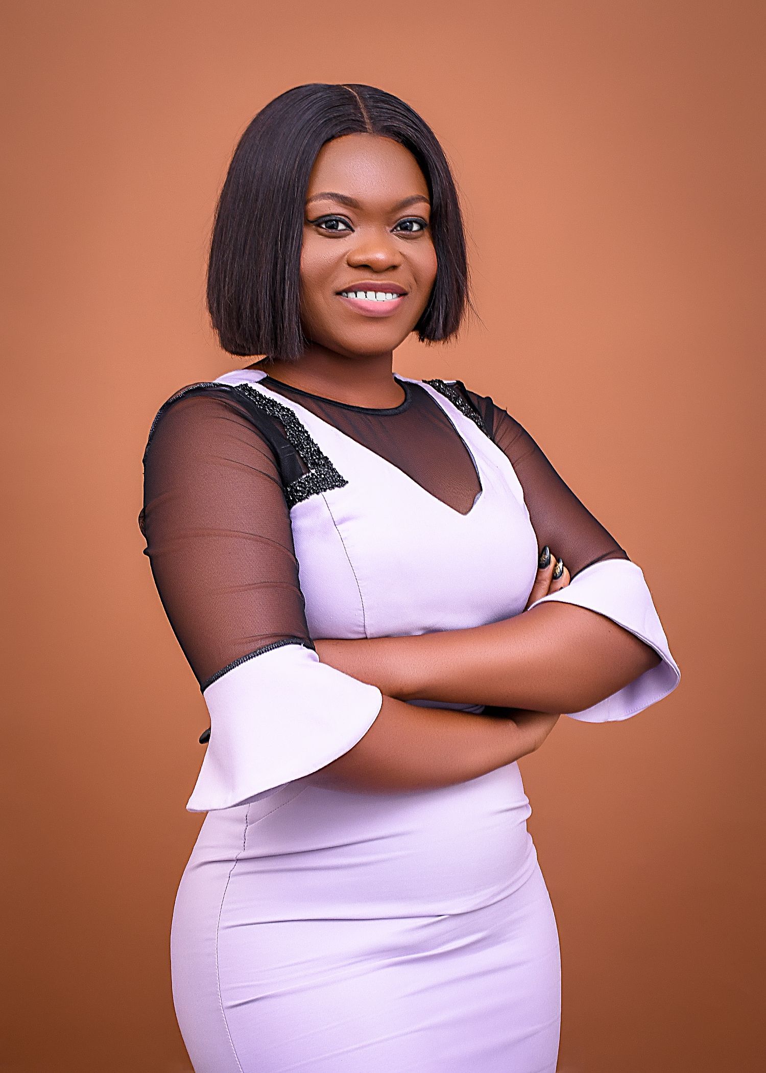 A woman in a white dress is standing with her arms crossed and smiling.